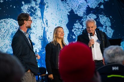 Three people on a stage with the back of some heads in the foreground