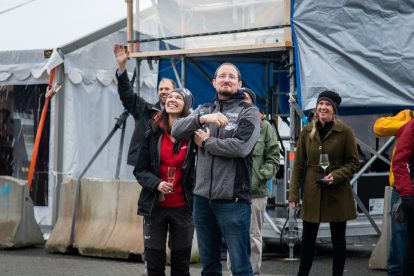 People waving in front of a tent and scaffolding