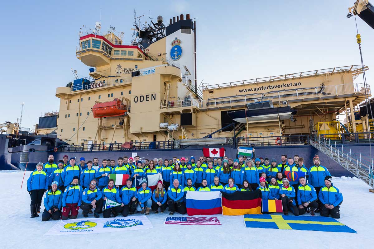 Group foto of scientists all wearing blue jackets on a ice flow in front of the research ice breaker Oden