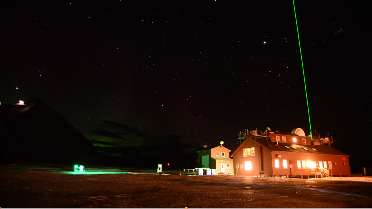 A house brightly lit at night with a green laser coming from it in the Arctic.