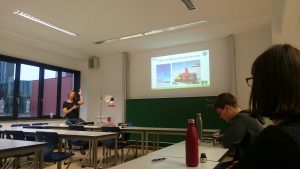 A lecture hall with black boards in the background and a person giving a presentation