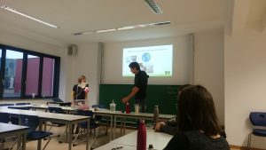 A lecture hall with black boards in the background and two people giving a presentation and showing experiments