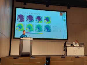 A person giving a talk on a podium with a large presentation behind them.