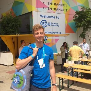 A person in a blue shirt with a tote bag in front of tables outside a conference venue