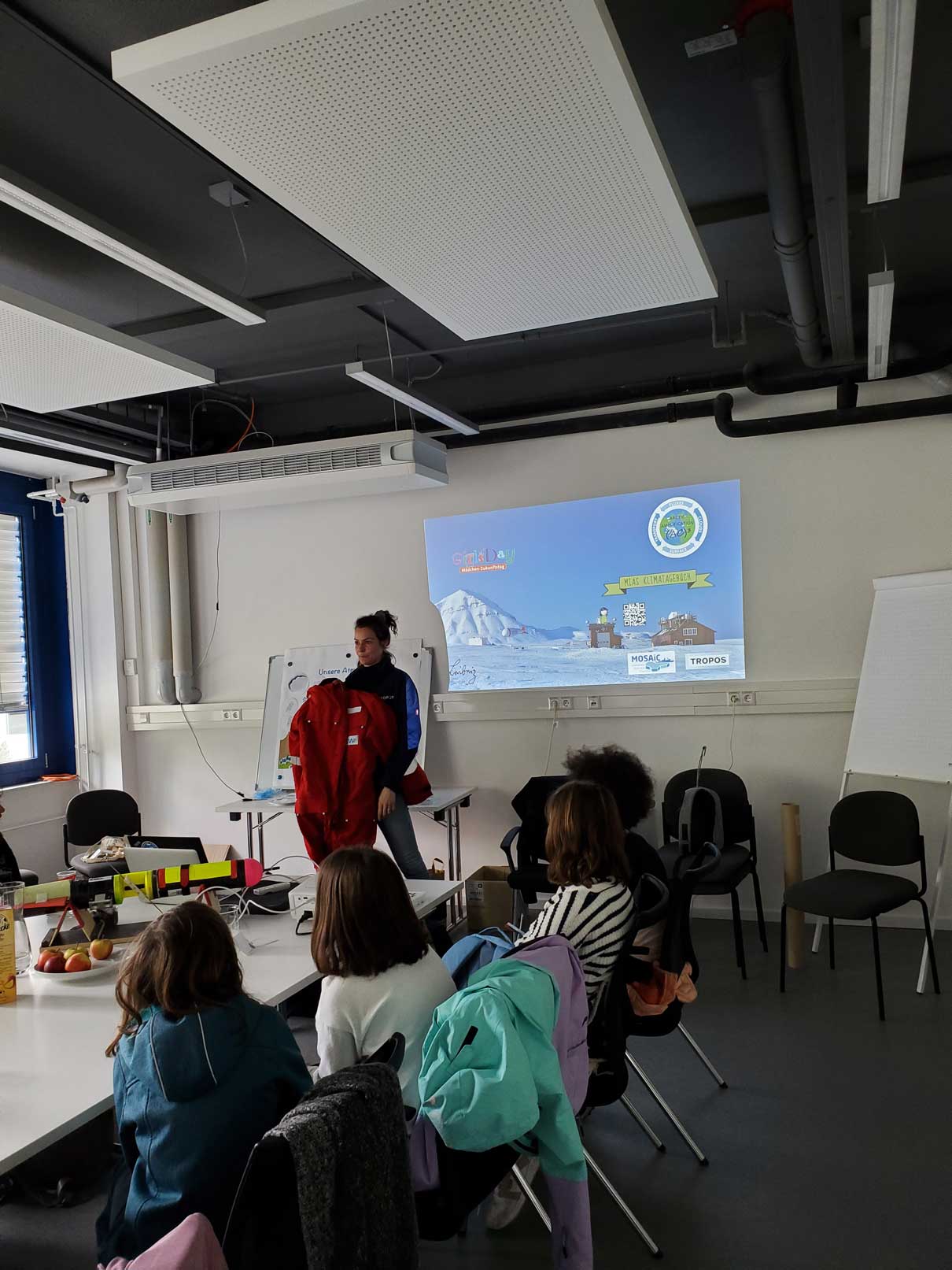 A scientist showing an Arctic survival suit in front of a group of young girls sitting at a conference table