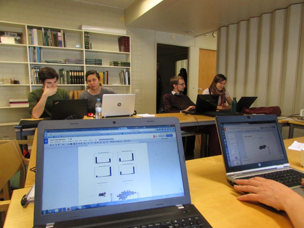 View over a laptop into a room full of people sitting in front of laptops