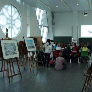 Room with a rose window and easels in the foreground and people standing in the background looking towards the opposite wall