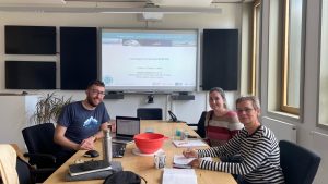 People sitting at a conference table looking into to the camera with a presentation behind them