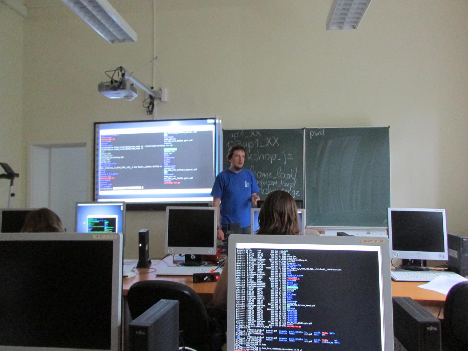 View over a laptop into a lecture room with a presentation of the LINUX console in the background