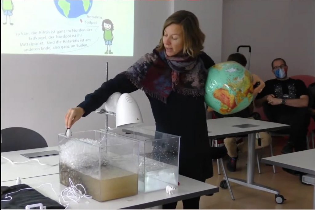 A person showing two small water tanks one with ice and one without while holding an inflatable globe