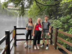 3 people on a wooden platform in front of a waterfall.