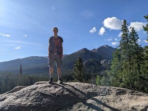 Person standing on a boulder with trees and mountains in the background